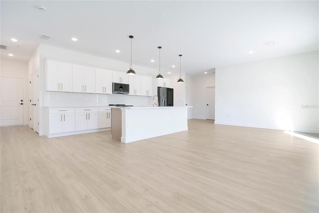 A bright, open-concept kitchen features white cabinetry, a central island, and light wood-look flooring — 469 MARION OAKS LANE, OCALA, FL