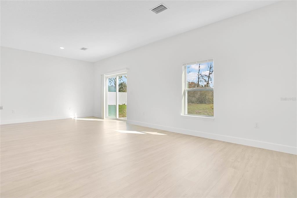 A bright, empty room with light wood-look flooring, white walls, a sliding door, and windows — 469 MARION OAKS LANE, OCALA, FL