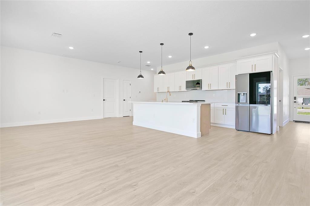 A bright, open-concept kitchen features white cabinetry, a center island, and light wood-look flooring — 469 MARION OAKS LANE, OCALA, FL