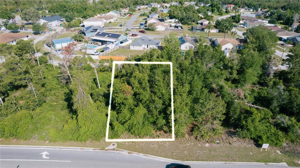 An aerial view shows a rectangular, tree-covered vacant lot bordered by a road and houses — 1672 CATALINA BOULEVARD, DELTONA, FL