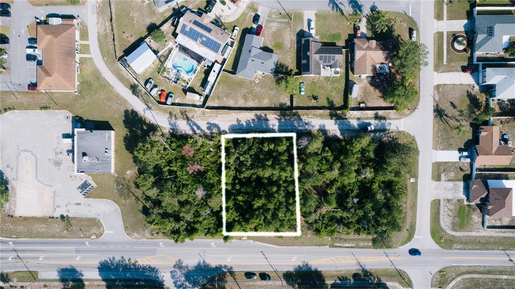 An aerial view shows a rectangular, wooded vacant lot outlined in white near a road — 1672 CATALINA BOULEVARD, DELTONA, FL