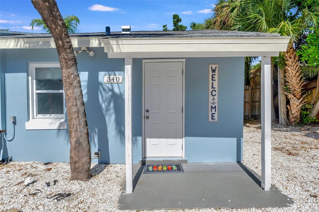The exterior of a light blue house features a white front door and a covered porch — 340 78TH AVENUE, ST PETE BEACH, FL