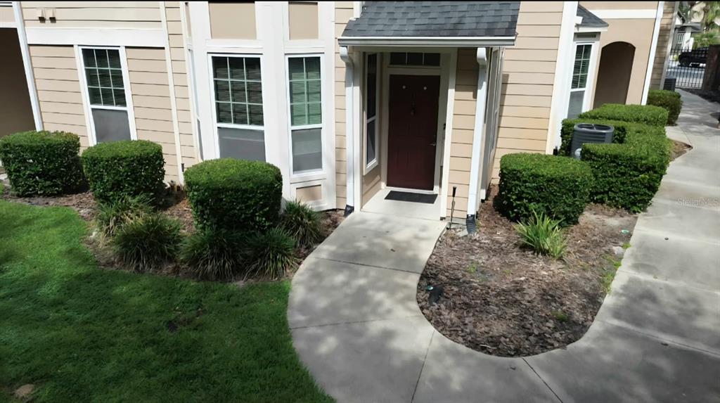 A tan exterior of a multi-story building features a red front door and landscaping — 1101 VINTAGE VILLAGE LANE UNIT 110, OCOEE, FL
