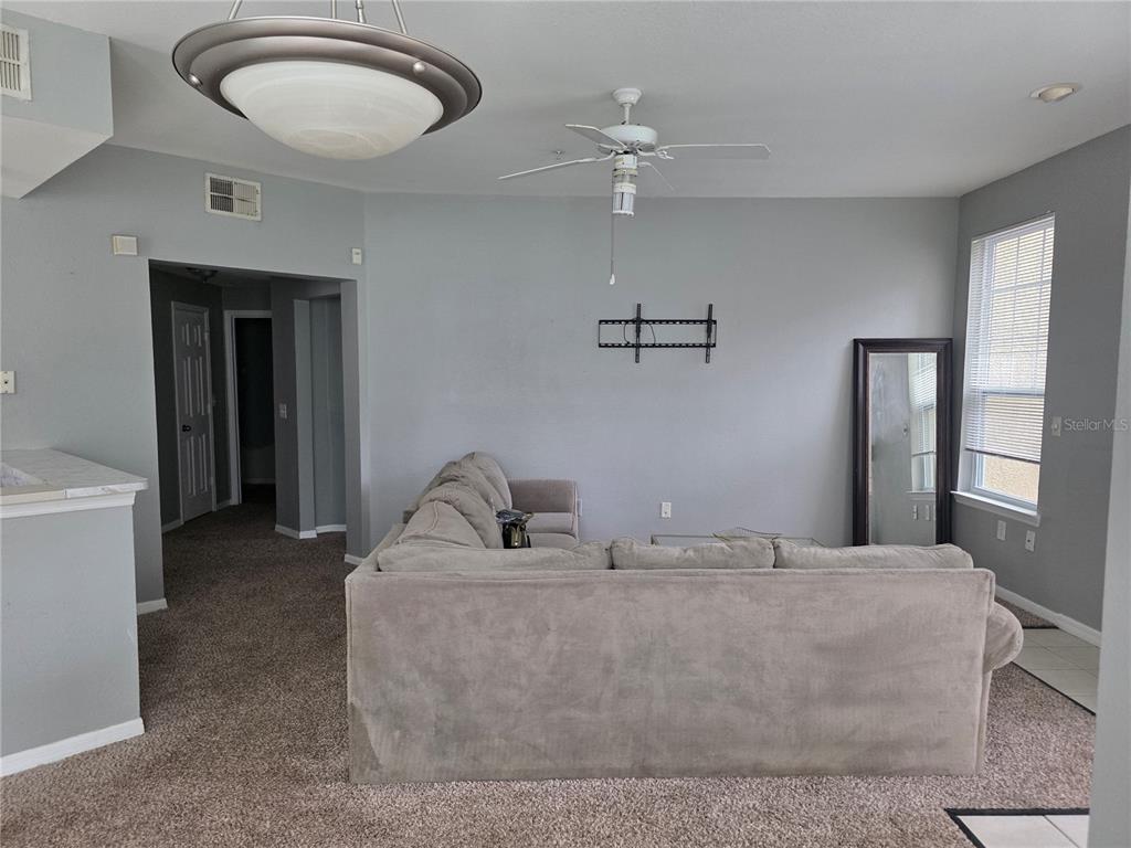 A living room features a large sectional sofa, a wall-mounted television bracket, and carpeted flooring — 1101 VINTAGE VILLAGE LANE UNIT 110, OCOEE, FL