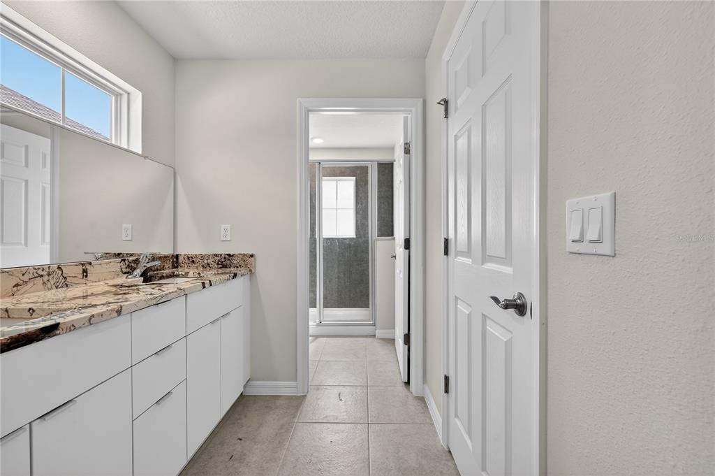 A bathroom features a granite-topped vanity, white cabinets, tile flooring, and a doorway to a shower — 172 HOLLY VILLAGE DRIVE, DAVENPORT, FL