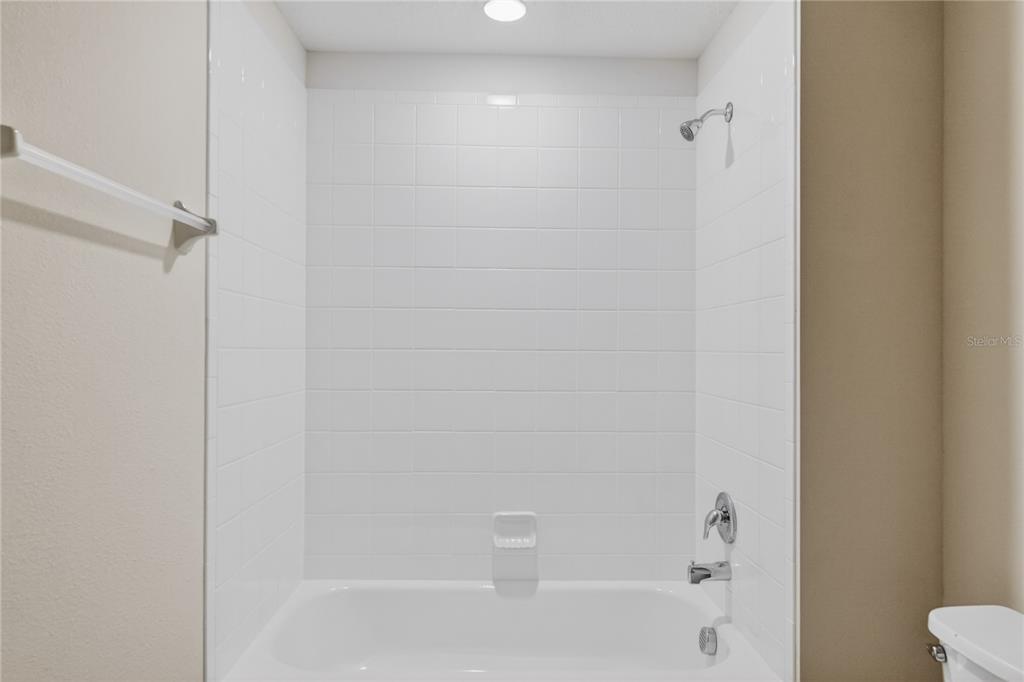 A white tiled bathtub and shower combination with chrome fixtures in a bathroom — 172 HOLLY VILLAGE DRIVE, DAVENPORT, FL