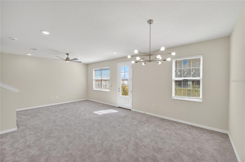 An empty room with gray carpet, a ceiling fan, a modern chandelier, and a door — 172 HOLLY VILLAGE DRIVE, DAVENPORT, FL