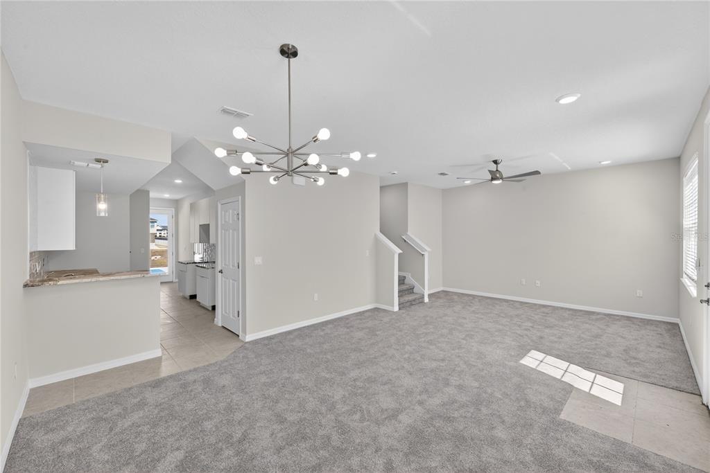 An open-concept living room features gray carpeting, a modern chandelier, and an adjacent kitchen area — 172 HOLLY VILLAGE DRIVE, DAVENPORT, FL