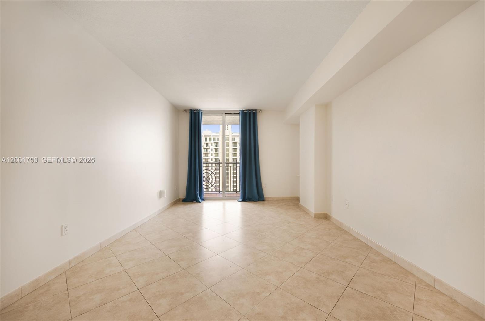 An empty room features beige tile flooring, white walls, and a balcony with blue curtains — 357 Almeria Ave # 1507, Coral Gables FL 33134, CORAL GABLES, FL