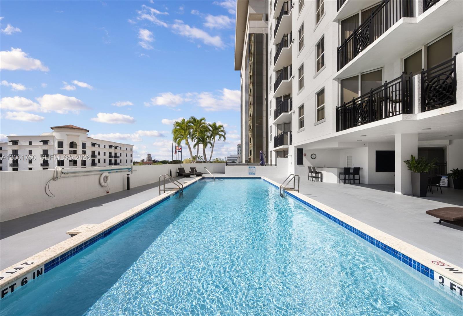 A rectangular swimming pool sits on a terrace next to a multi-story residential building — 357 Almeria Ave # 1507, Coral Gables FL 33134, CORAL GABLES, FL