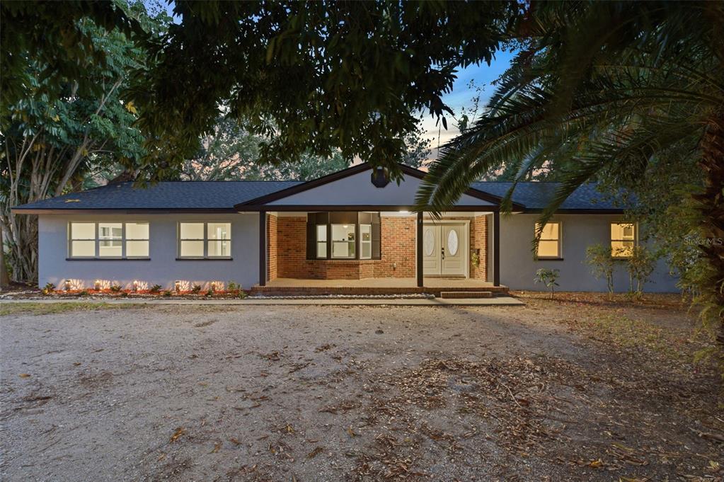 A single-story house with a brick facade, covered porch, and gravel driveway at dusk — 3084 SPIREA STREET, SARASOTA, FL