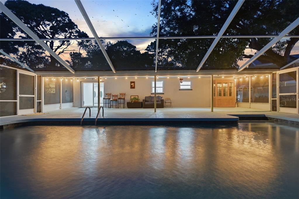 A swimming pool sits in front of a covered patio with string lights and furniture — 3084 SPIREA STREET, SARASOTA, FL