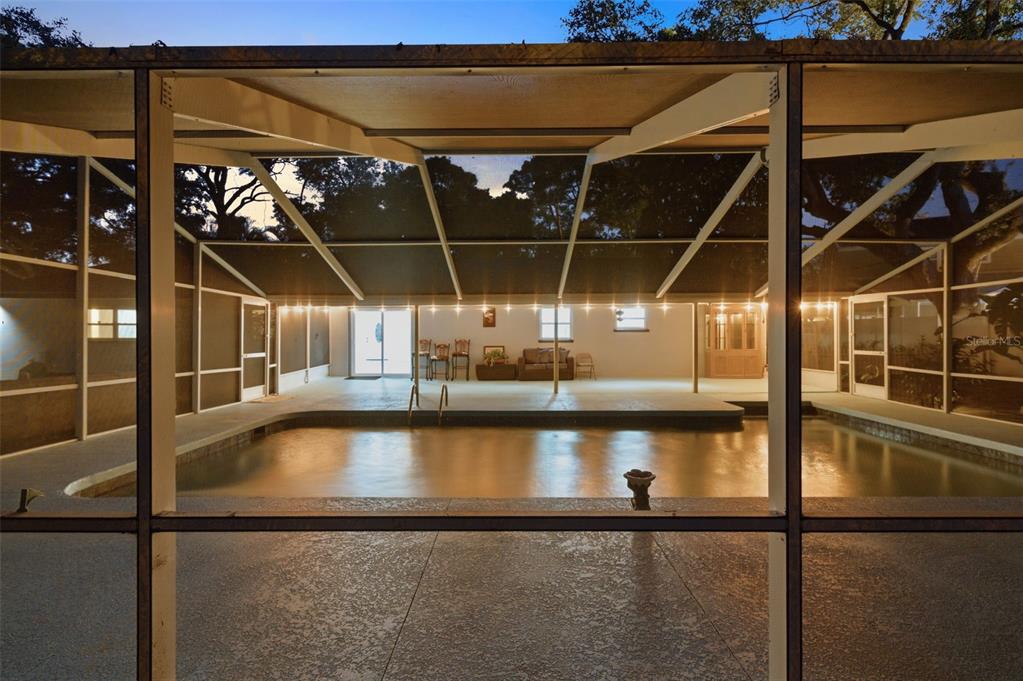 A screened-in patio features a swimming pool and a covered seating area at night — 3084 SPIREA STREET, SARASOTA, FL