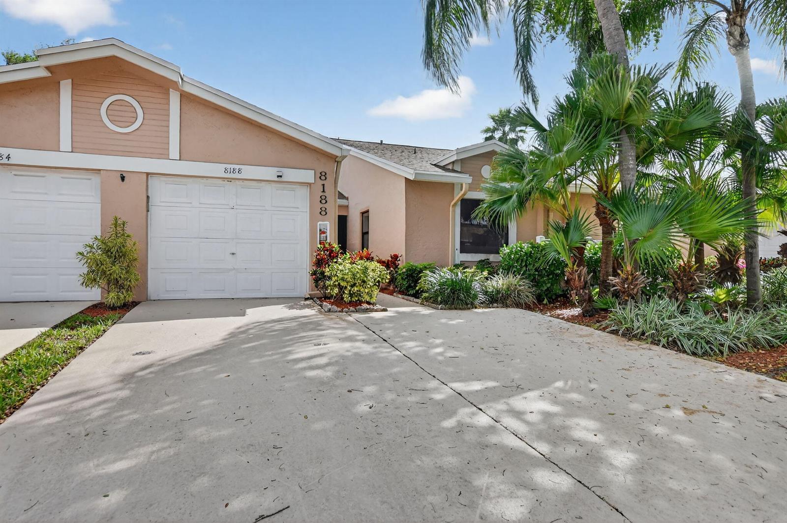 A peach-colored single-story house features a white garage door, a concrete driveway, and tropical landscaping — 8188 Summerbreeze Lane, Boca Raton FL 33496, BOCA RATON, FL