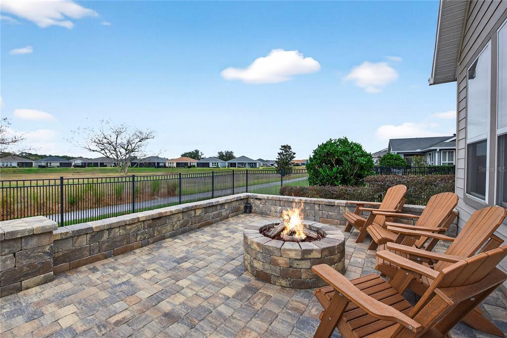 A stone patio features a fire pit, wooden chairs, and a metal fence overlooking houses — 5575 NW 43RD LANE ROAD, OCALA, FL