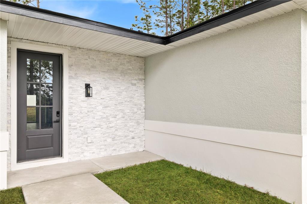A gray front door with glass panes sits next to a white stone accent wall — 2421 W LANDMARK DRIVE, CITRUS SPRINGS, FL