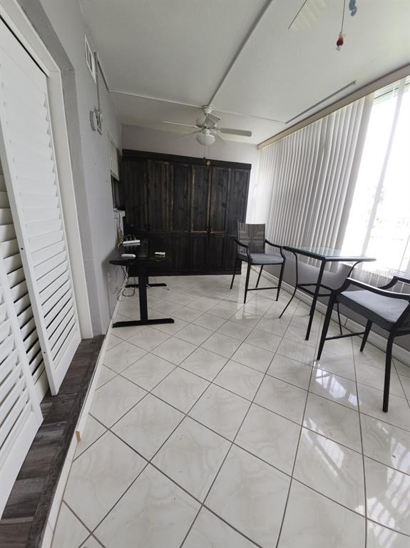 A sunroom features white tile flooring, a ceiling fan, a dark storage unit, and furniture — 1819 SHORE DRIVE S UNIT 217, SOUTH PASADENA, FL