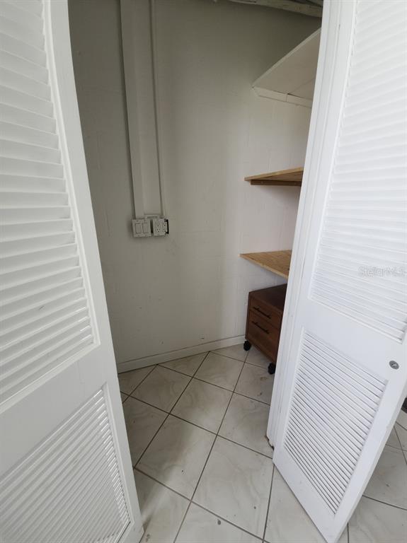 A closet with louvered doors, tiled flooring, wooden shelves, and wall-mounted electrical outlets — 1819 SHORE DRIVE S UNIT 217, SOUTH PASADENA, FL