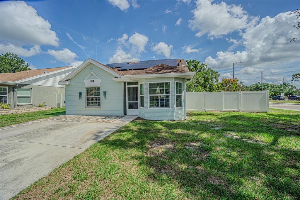 A light green single-story house with a paved driveway, solar panels, and a white fence — 7601 LIMEBURY COURT, TAMPA, FL