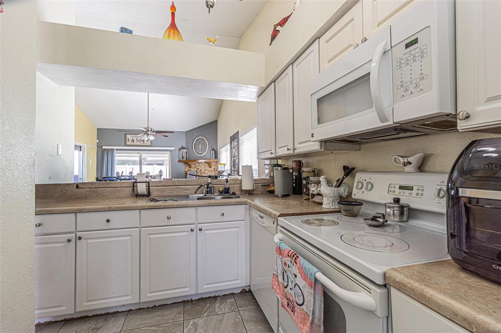 A kitchen features white cabinets, laminate countertops, a white stove, and a pass-through window — 7601 LIMEBURY COURT, TAMPA, FL