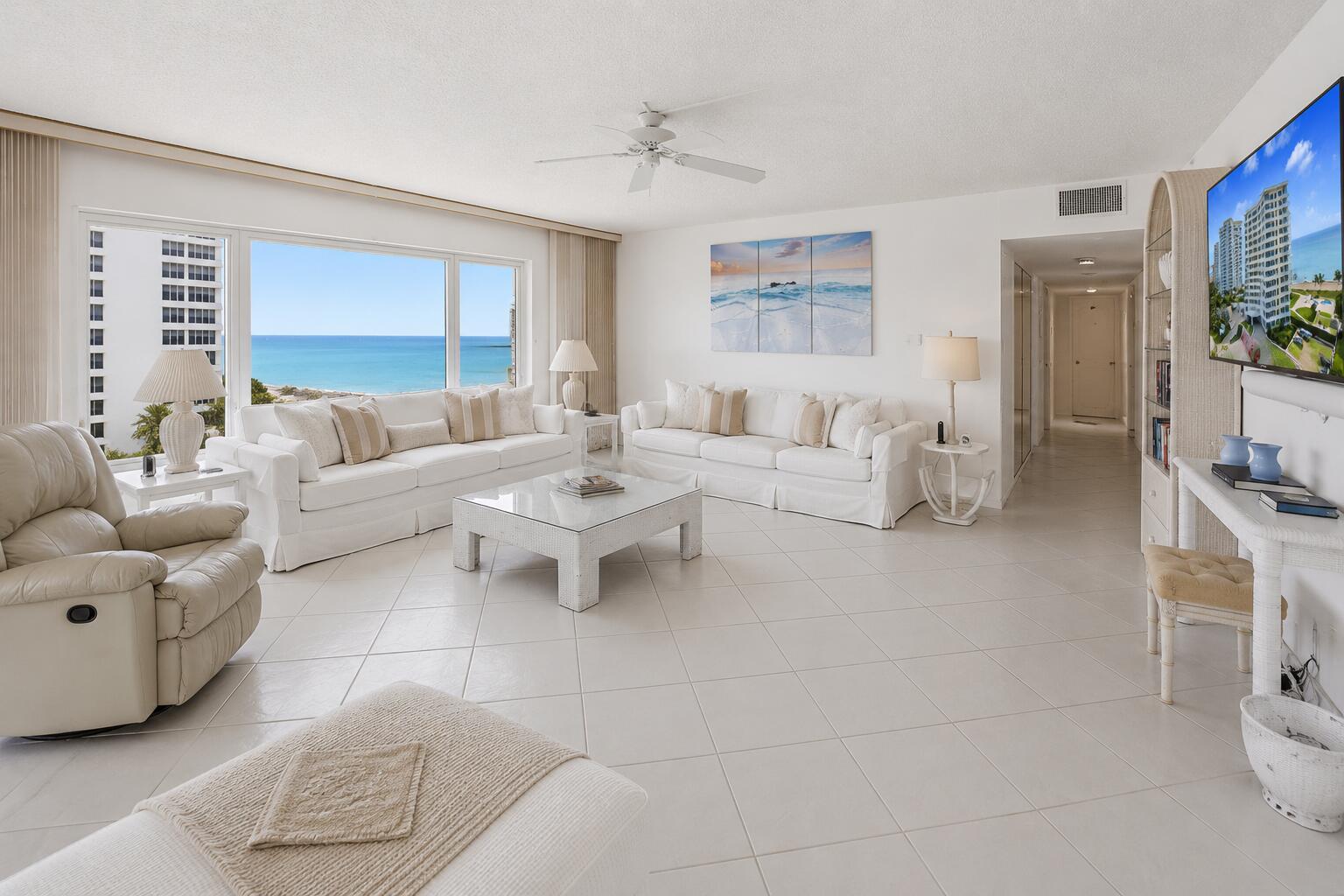 A bright living room features white furniture, tile flooring, and a large window overlooking the ocean — 600 S Ocean Boulevard # 6010, Boca Raton FL 33432, BOCA RATON, FL