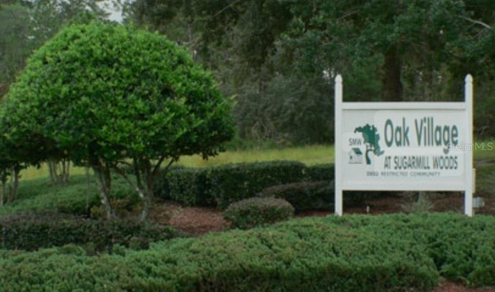 A white sign for Oak Village at Sugarmill Woods stands beside a large, manicured green tree — 11 SCABIOSA COURT, HOMOSASSA, FL