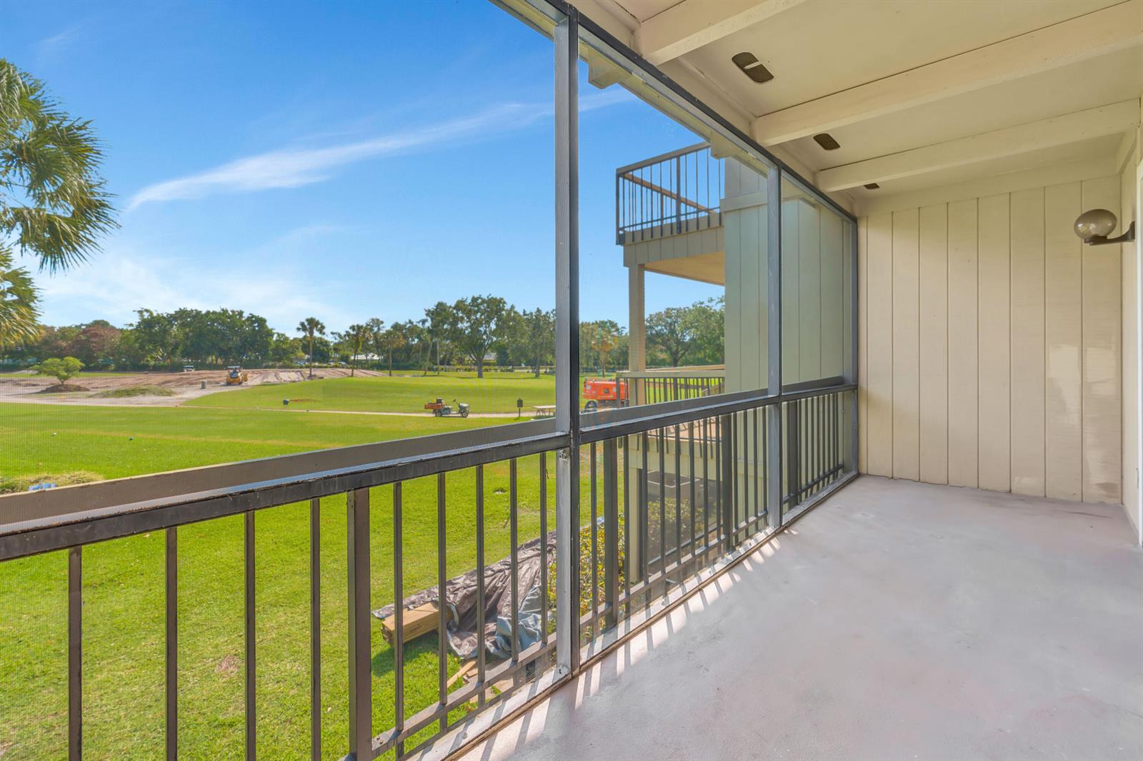 A screened-in balcony overlooks a grassy golf course with construction equipment in the distance — 18419 SE Wood Haven Lane # B, Tequesta FL 33469, TEQUESTA, FL
