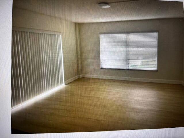 An empty room features light wood-look flooring, vertical blinds on a sliding door, and horizontal blinds — 4164 Inverrary Drive # 702, Lauderhill FL 33319, LAUDERHILL, FL