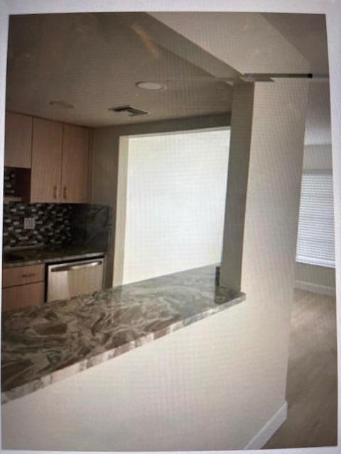 A kitchen features light wood cabinets, a patterned backsplash, and a stone breakfast bar — 4164 Inverrary Drive # 702, Lauderhill FL 33319, LAUDERHILL, FL