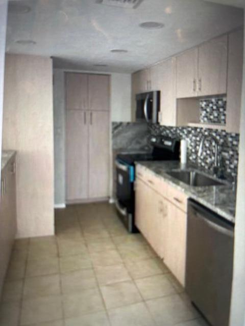 A galley kitchen features light wood cabinets, stainless steel appliances, and a tiled backsplash — 4164 Inverrary Drive # 702, Lauderhill FL 33319, LAUDERHILL, FL