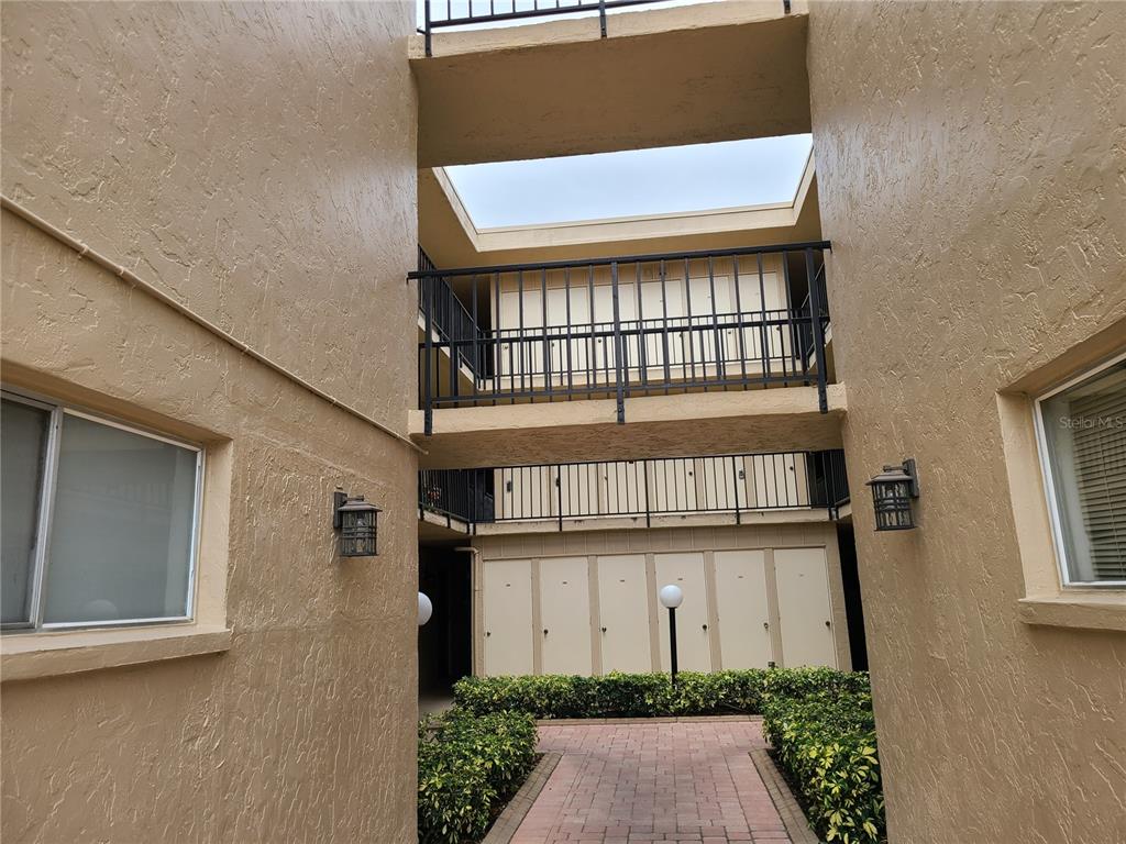 A paved walkway leads between two tan stucco buildings with metal railings and exterior lighting — 2763 WOODGATE LANE UNIT 204, SARASOTA, FL
