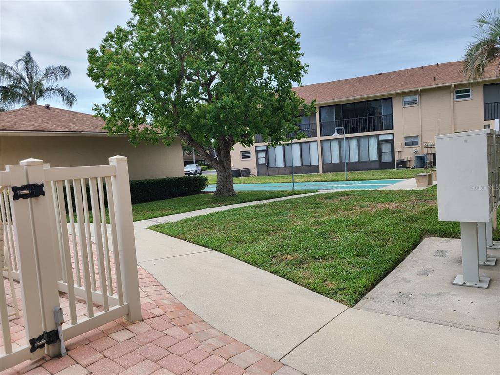 A view of a sidewalk, lawn, large tree, and a multi-story apartment building — 2763 WOODGATE LANE UNIT 204, SARASOTA, FL
