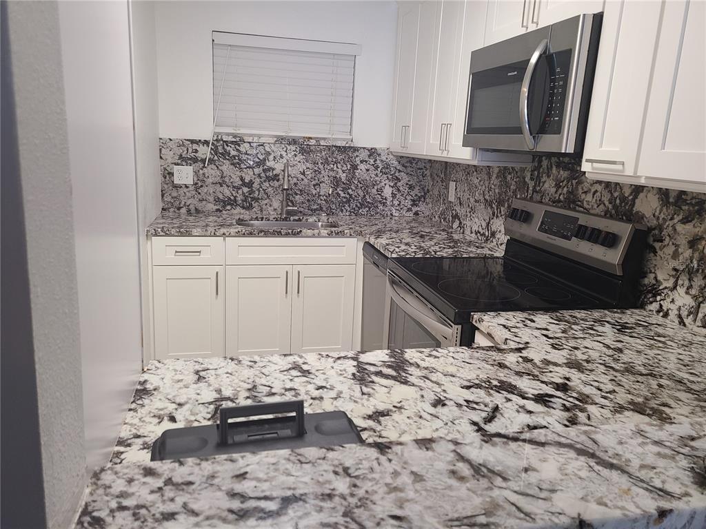A kitchen features white cabinets, granite countertops, a stainless steel microwave, and a glass-top stove — 2763 WOODGATE LANE UNIT 204, SARASOTA, FL