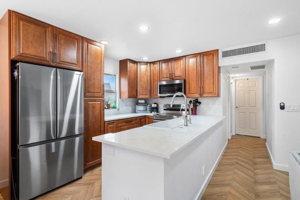 A kitchen features wood cabinets, stainless steel appliances, a white island, and herringbone wood flooring — 156 Seville, Delray Beach FL 33446, DELRAY BEACH, FL