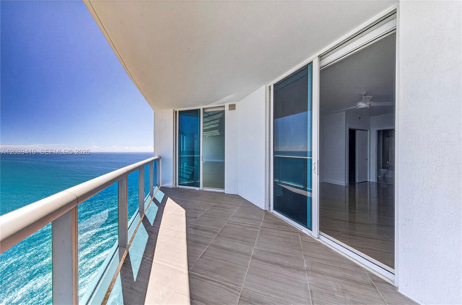 A balcony with tile flooring and glass railings overlooks the ocean through sliding glass doors — 2711 S OCEAN DR # 3102, Hollywood FL 33024, HOLLYWOOD, FL