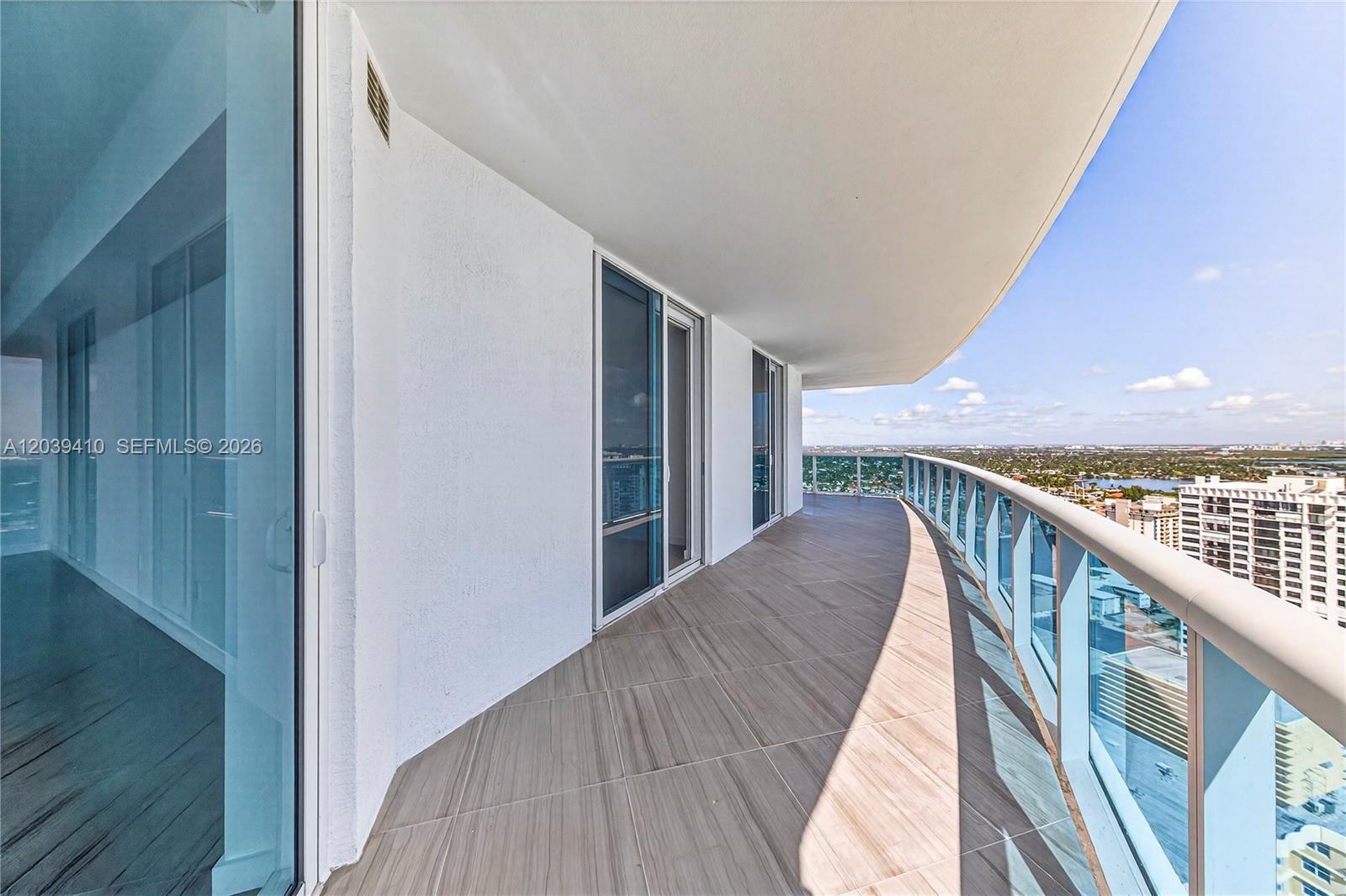 A curved balcony with wood-look tile flooring and a glass railing overlooks a city skyline — 2711 S OCEAN DR # 3102, Hollywood FL 33024, HOLLYWOOD, FL