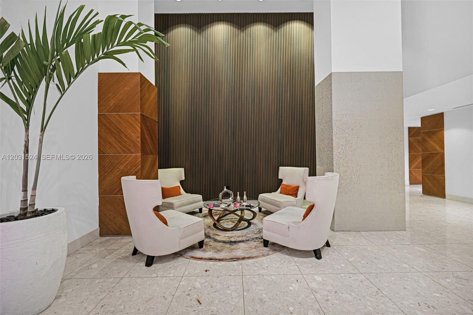 A modern lobby seating area features four white armchairs, a glass coffee table, and wood-paneled walls — 3801 Collins Ave # 1102, Miami Beach FL 33140, MIAMI BEACH, FL