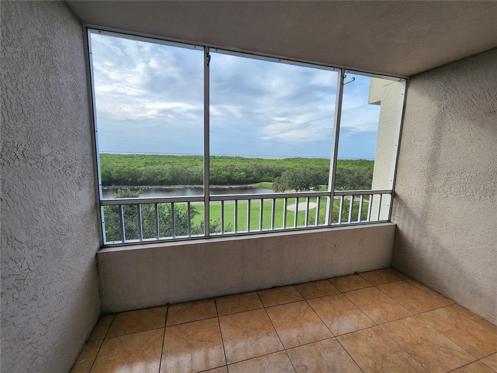 A tiled balcony with a screened enclosure overlooks a golf course and distant water — 2333 FEATHER SOUND DRIVE UNIT A607, CLEARWATER, FL