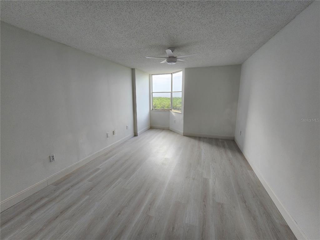 An empty room with light wood-look flooring, white walls, and a window overlooking greenery — 2333 FEATHER SOUND DRIVE UNIT A607, CLEARWATER, FL