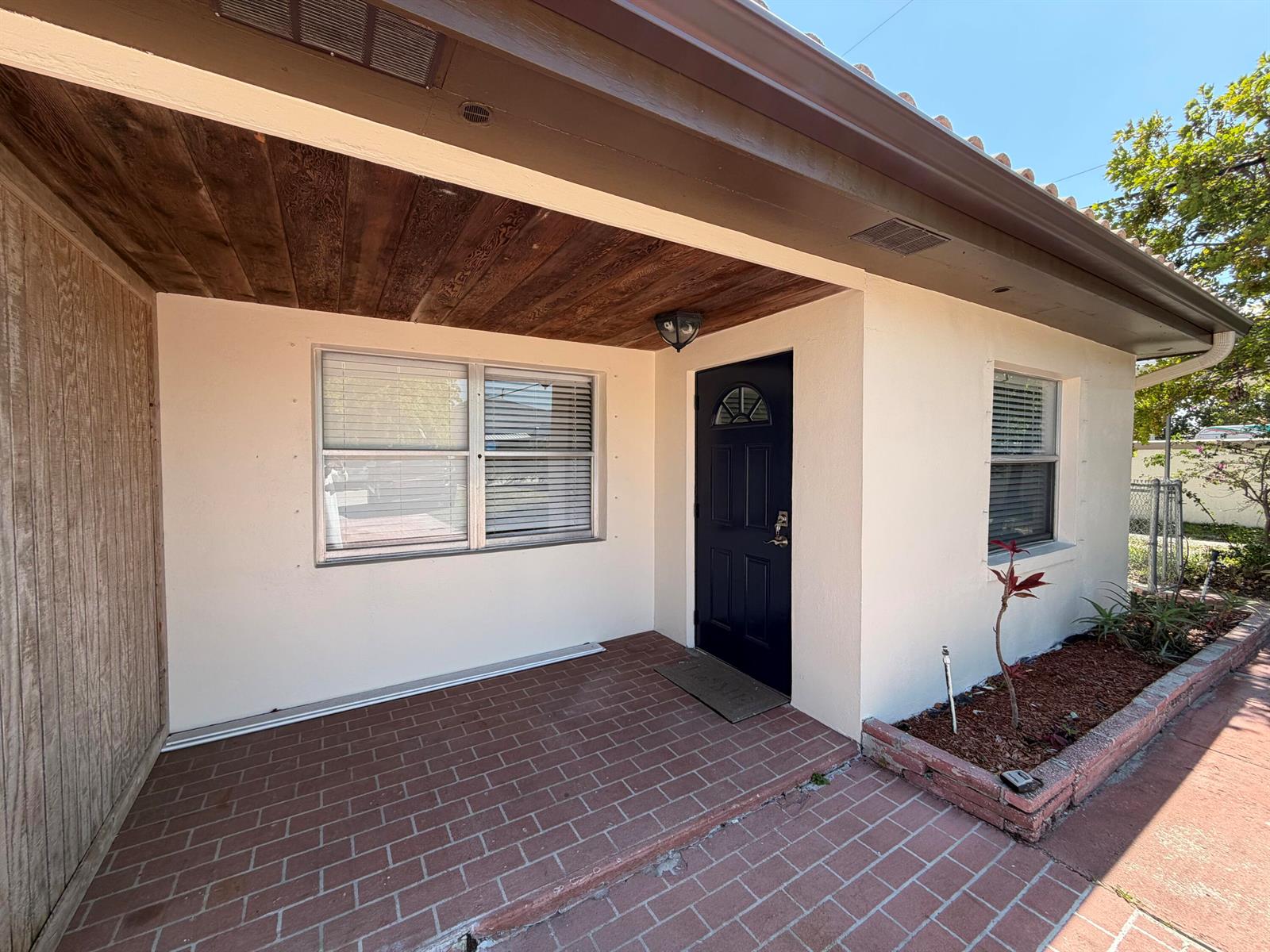 A brick patio leads to a dark blue front door under a wood-paneled porch ceiling — 112 Prospect Road, Lantana FL 33462, LANTANA, FL