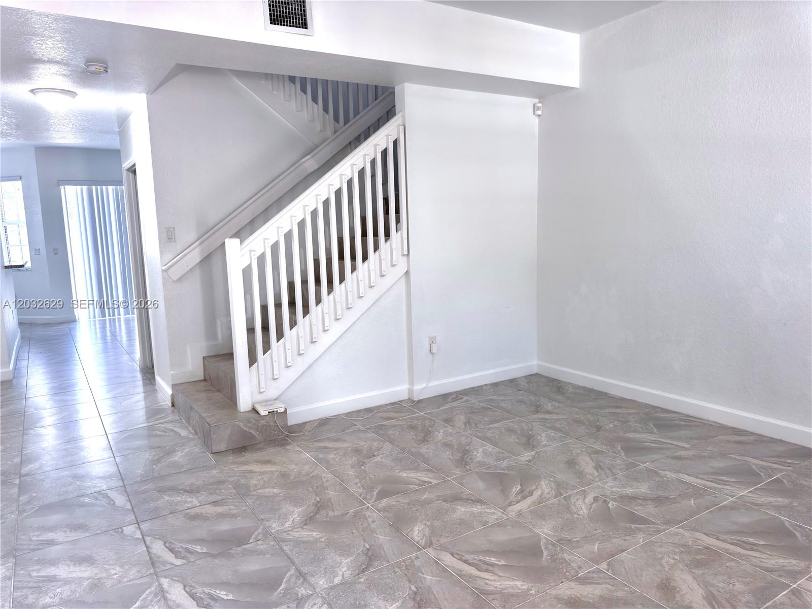 A room with gray tile flooring features a white staircase with a wooden railing — 7905 SW 120th Ave # 7905, Miami FL 33183, MIAMI, FL