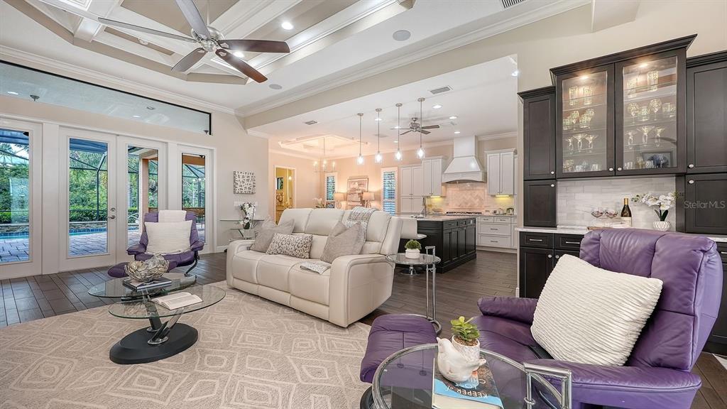 A living room with a white sofa, purple armchairs, and an open kitchen with dark cabinetry — 7640 HADDINGTON COVE, LAKEWOOD RANCH, FL
