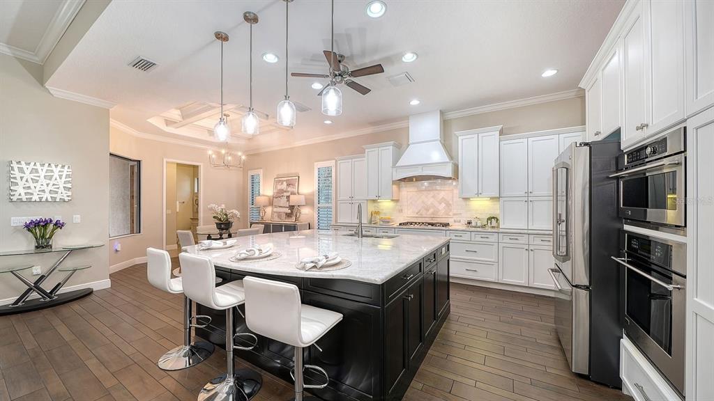 A modern kitchen features a large dark island, white cabinetry, and stainless steel appliances — 7640 HADDINGTON COVE, LAKEWOOD RANCH, FL