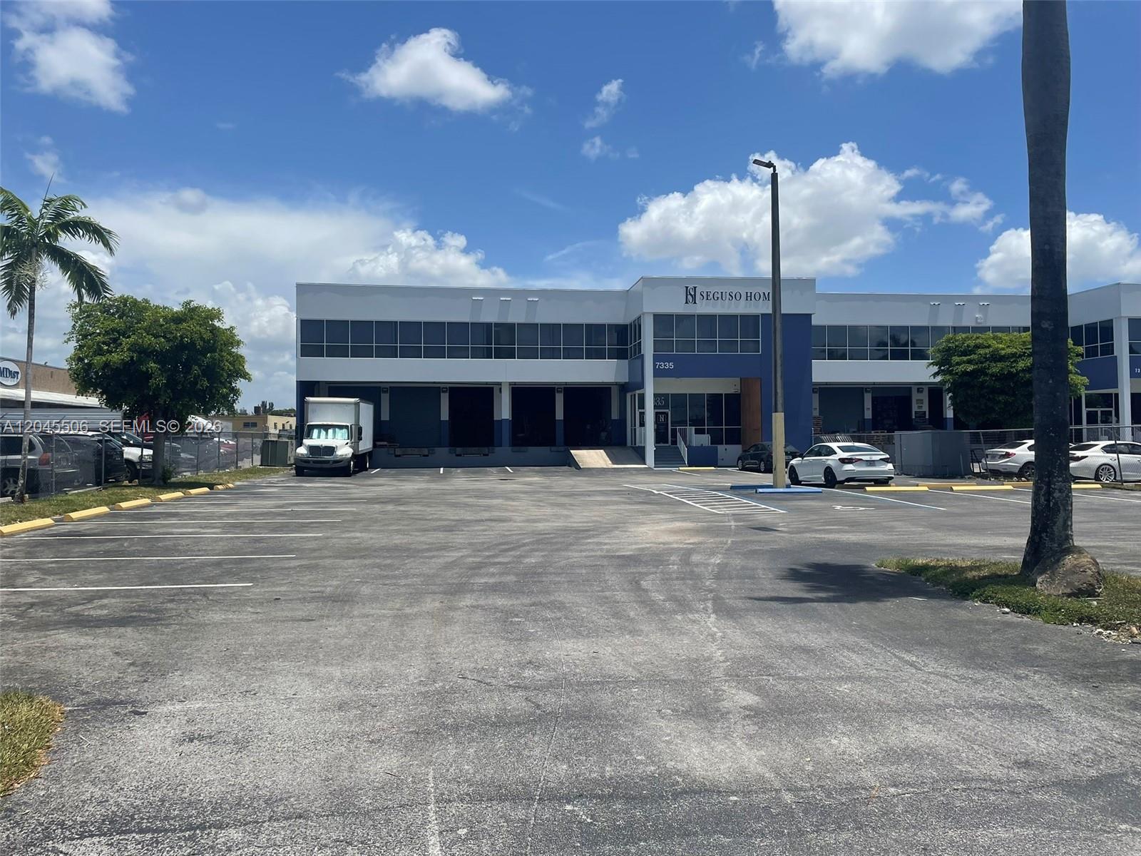 A commercial building features a large parking lot, loading docks, and a blue and white facade — FL