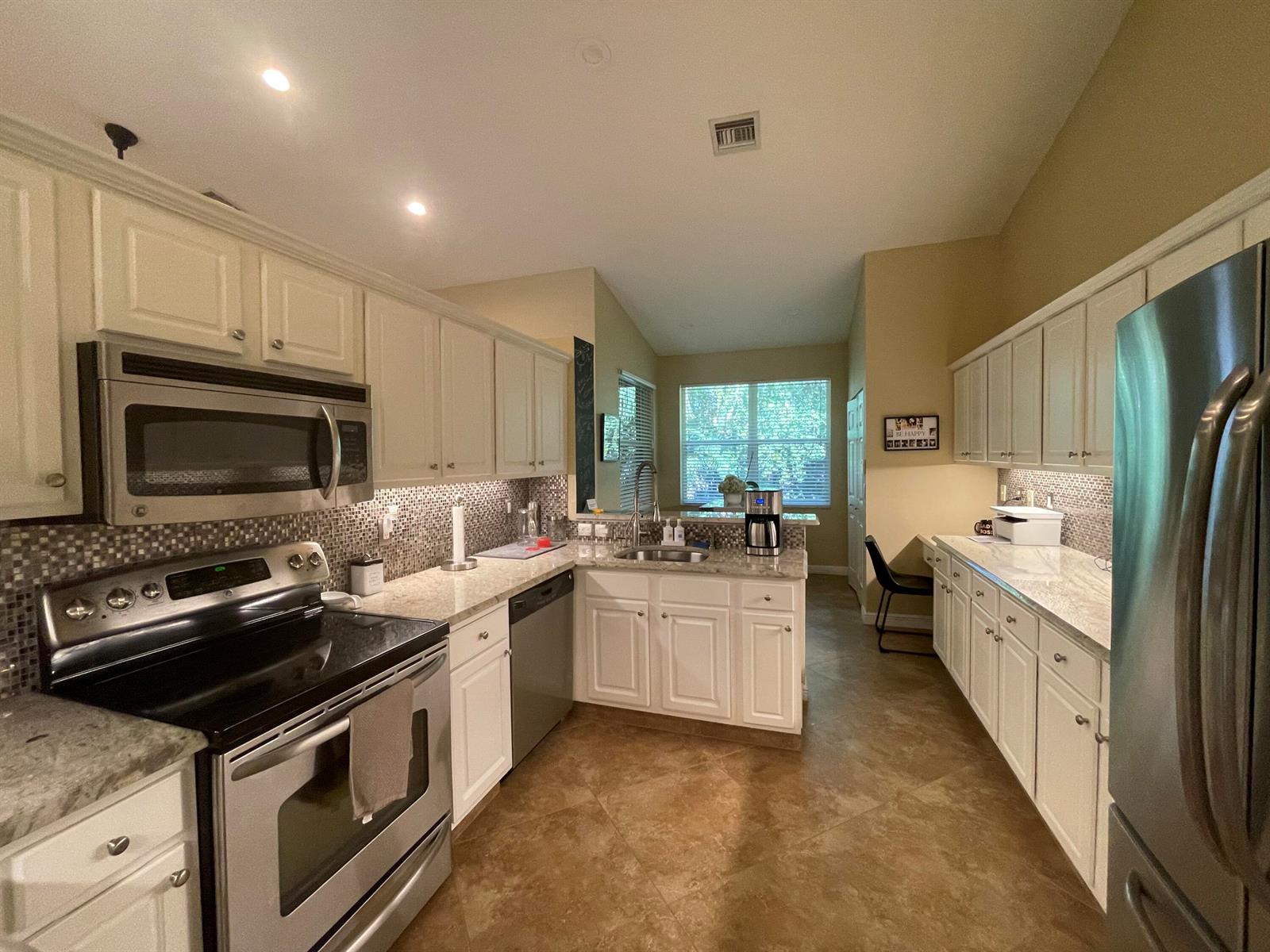 A kitchen features white cabinets, stainless steel appliances, granite countertops, and a mosaic tile backsplash — 16075 Sims Road # 203, Delray Beach FL 33484, DELRAY BEACH, FL