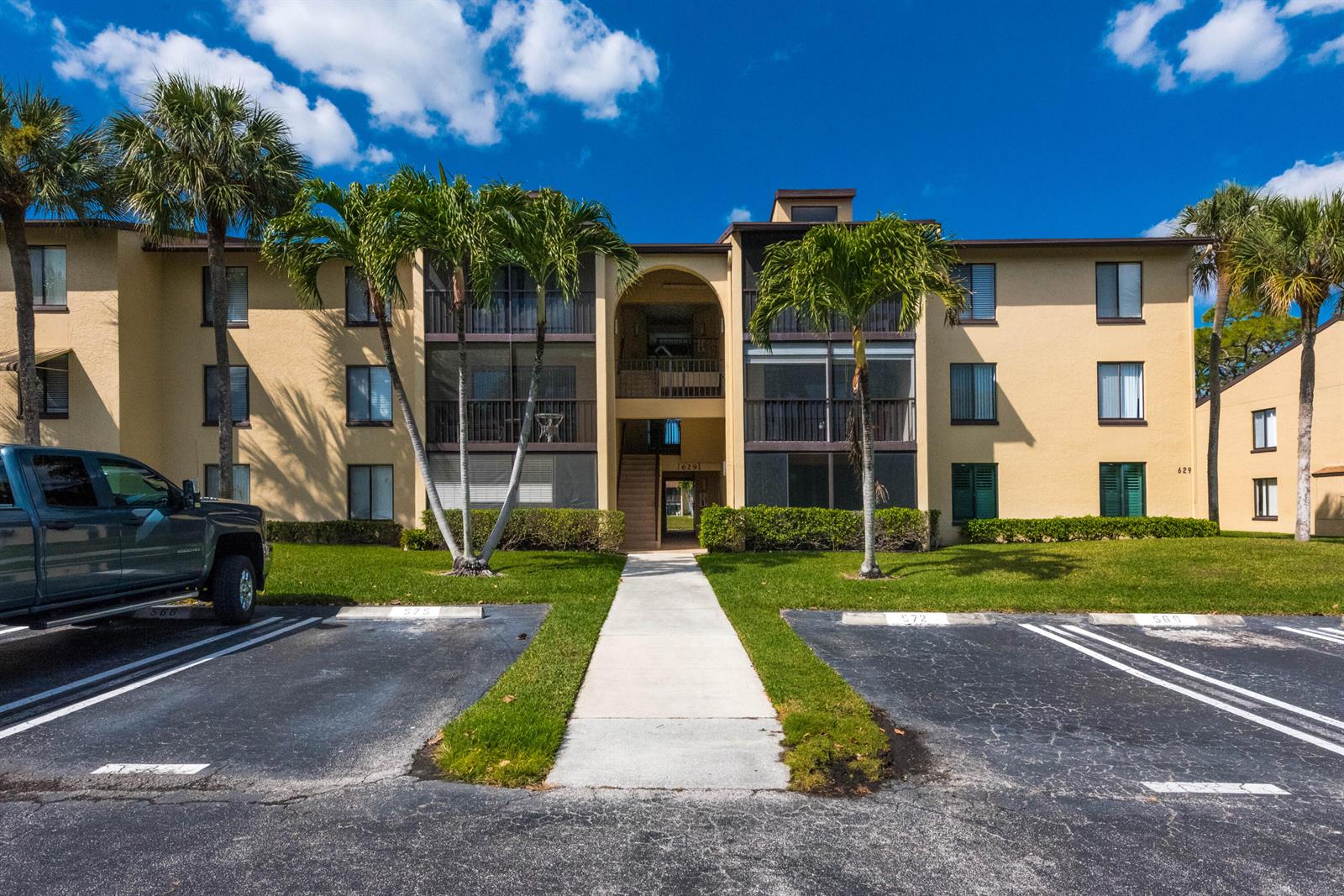 A three-story apartment building with a central arched entryway, screened balconies, and palm trees — 629 Sea Pine Way # D3, FL 33415, FL