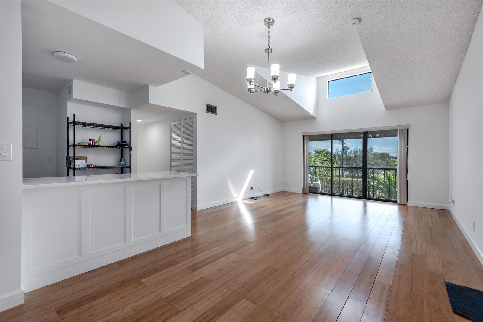 An open-concept living area features vaulted ceilings, a kitchen island, and sliding glass balcony doors — 629 Sea Pine Way # D3, FL 33415, FL