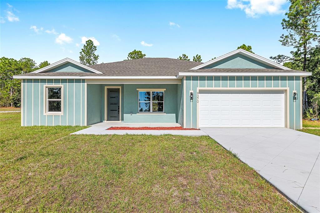 A single-story house with light blue board-and-batten siding, a white garage door, and a driveway — 9370 N DEL RIO WAY, CITRUS SPRINGS, FL