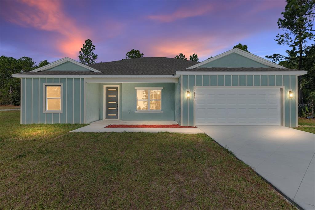 A single-story house with light blue board-and-batten siding and a two-car garage at dusk — 9370 N DEL RIO WAY, CITRUS SPRINGS, FL
