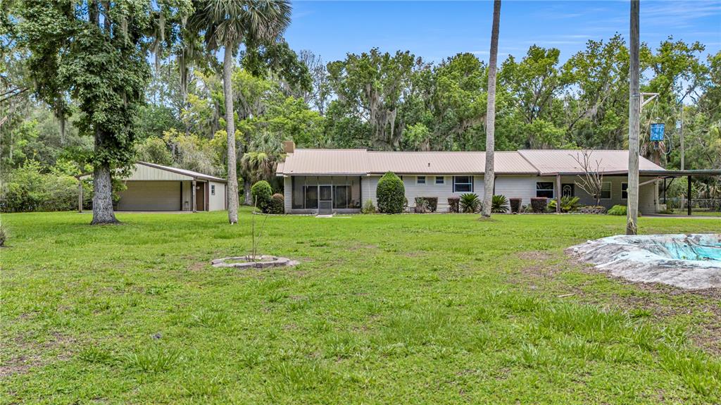 A single-story house with a metal roof and a detached garage sits on a lawn — 22308 BLUE CREEK LODGE ROAD, ASTOR, FL